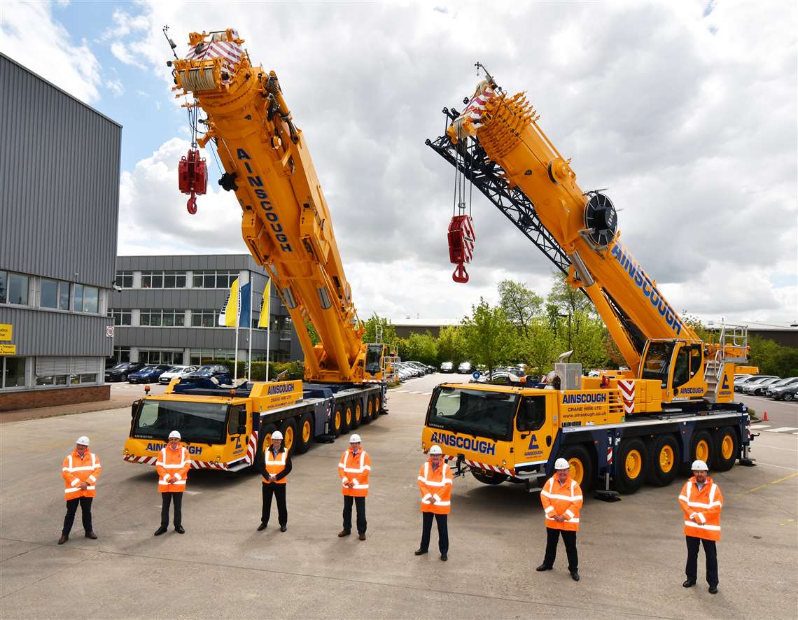 Two new yellow cranes, boom up, with a row of orange-clad blokes stood in front