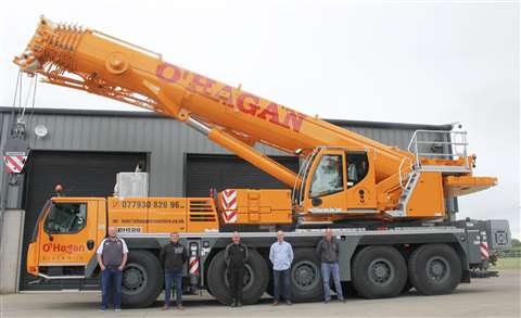 Side view of yellow five axle all terrain crane, boom raised slightly, people standing in front