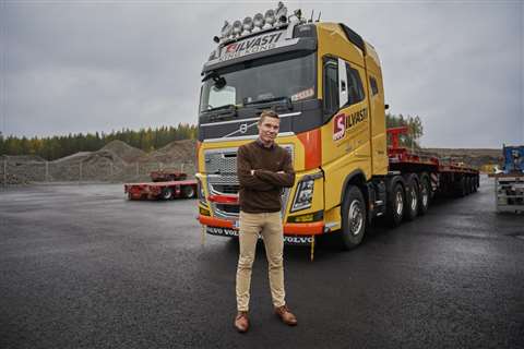 Ville, arms folded, standing in front of one of his yellow and red trucks