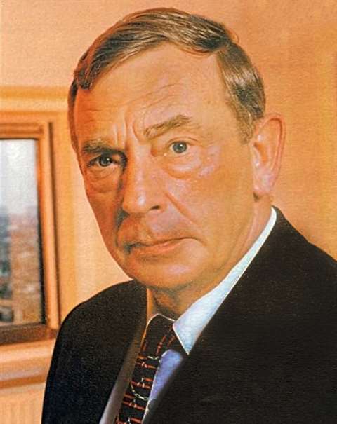Photo portrait of IJmker in a dark jacket and coloured tie standing in an office
