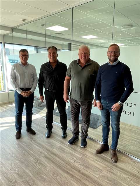 Four blokes lined up side by side looking happy in a glass office