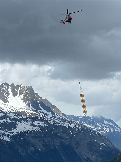 A helicopter transports part of a Potain MDT 109 crane over the French Alps